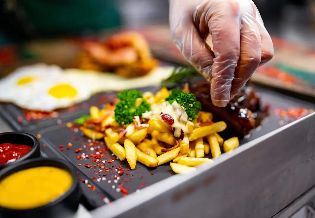 Chef garnishing fries with herbs and spices.